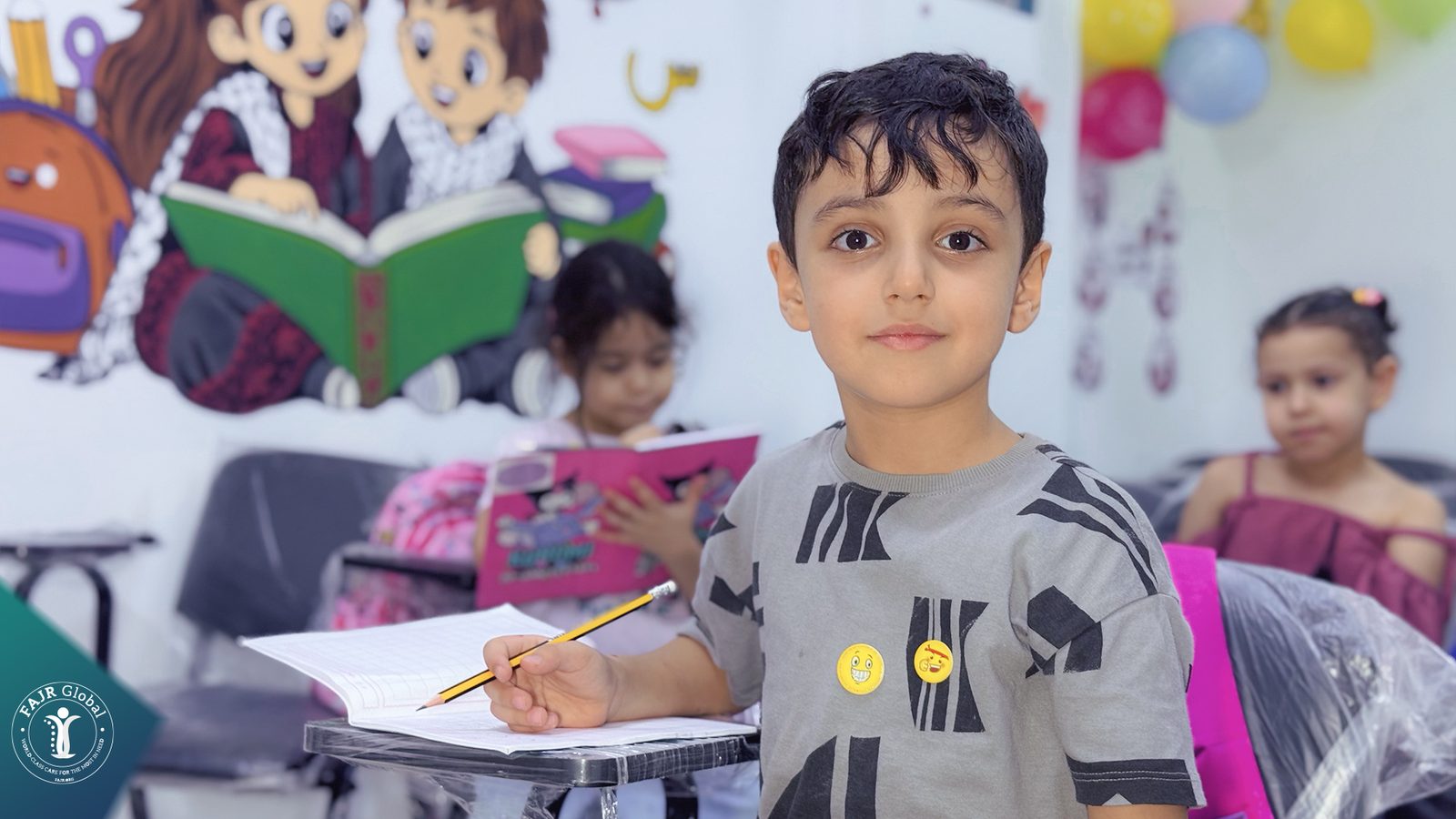 A young Palestinian boy holding his pencil at his desk