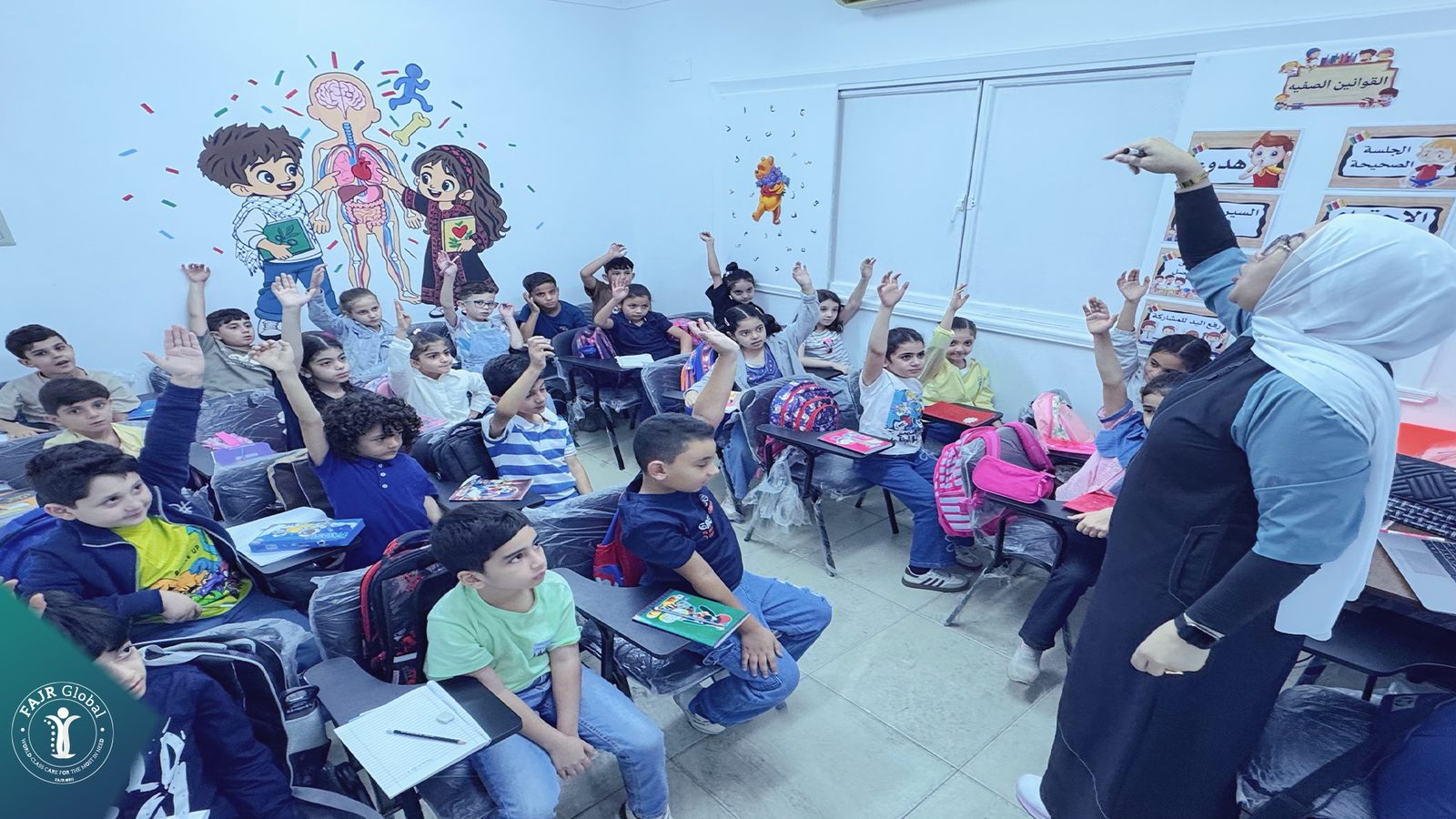A classroom of younger students raising their hands
