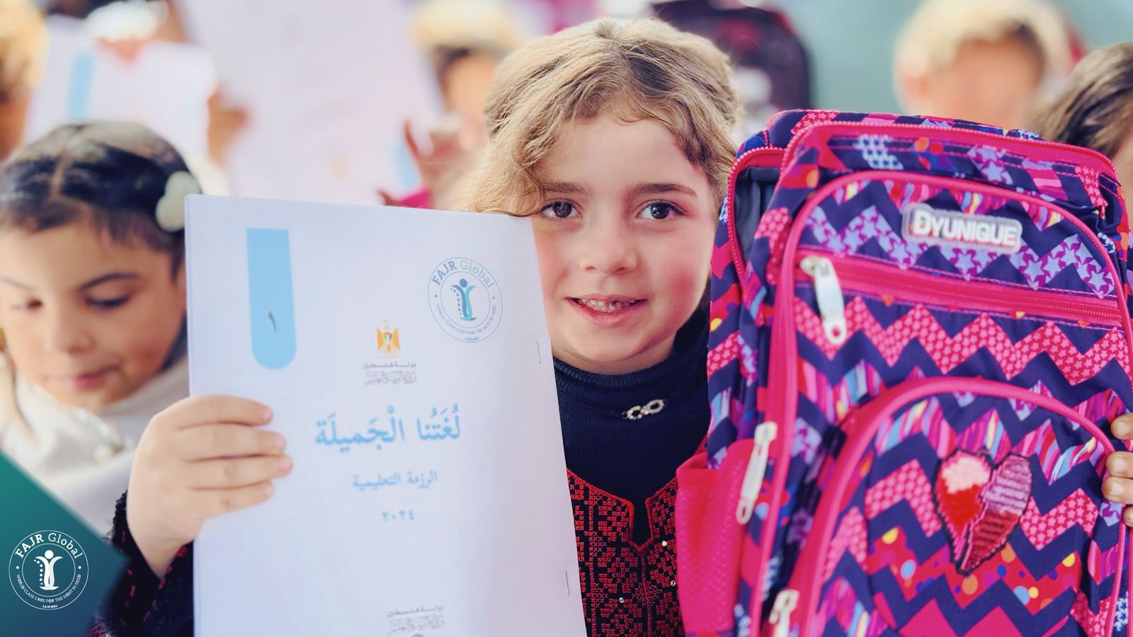 A girl smiles holding a new Arabic textbook and a pink school backpack