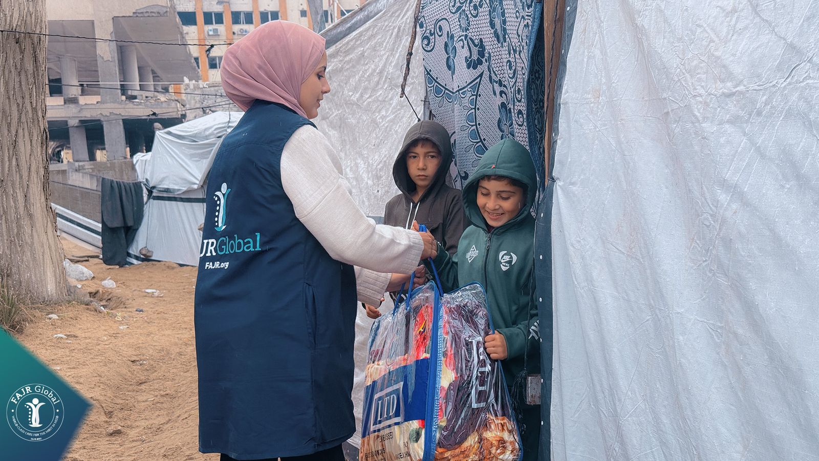A FAJR Global volunteer gives winter blankets to two children at their tent