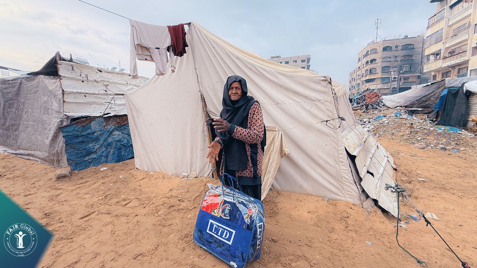 A woman in a displacement camp in Gaza stands beside her new winter blanket bag