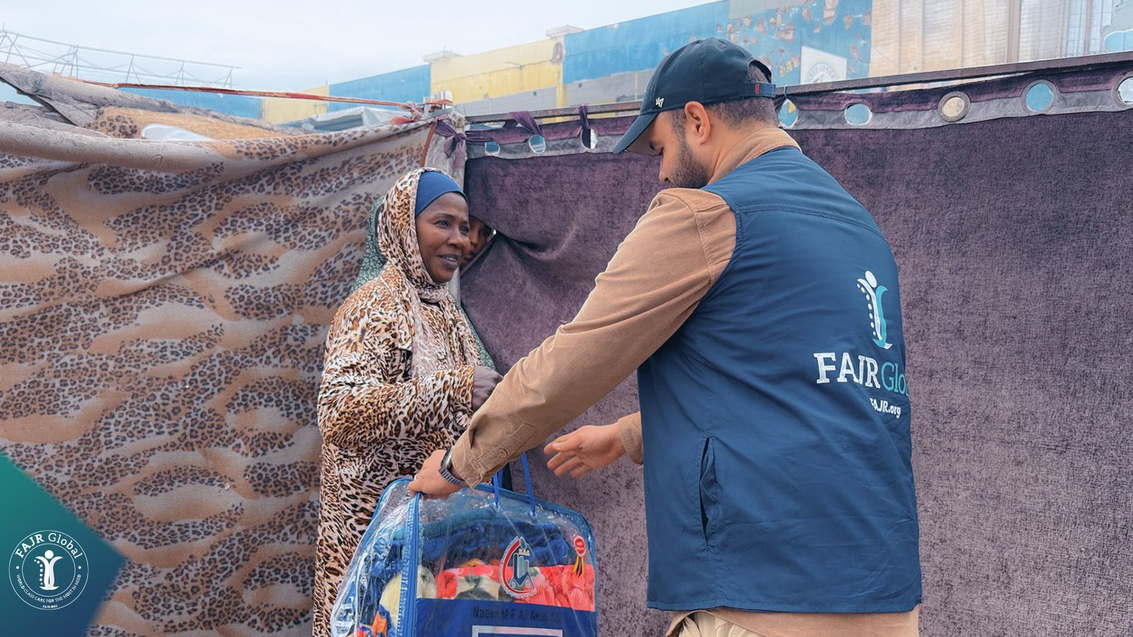 A FAJR Global volunteer hands a winter blanket bag to a woman