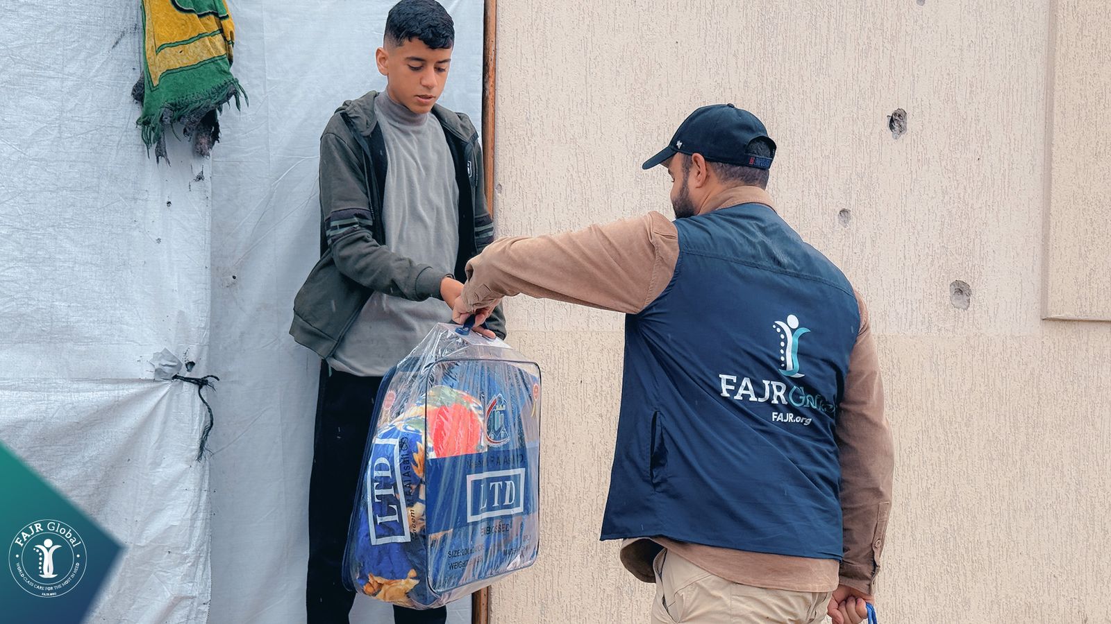 A FAJR Global volunteer hands a winter blanket bag to a young man