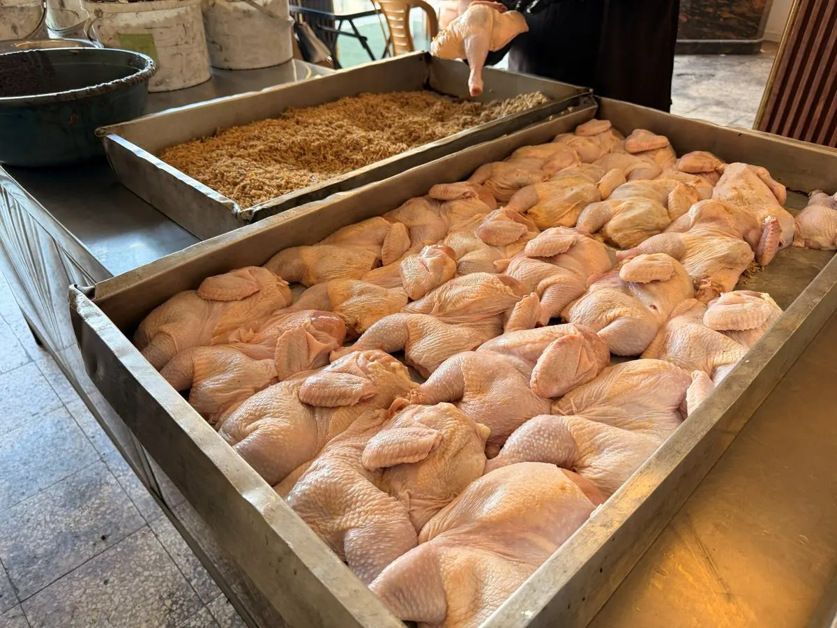 Large trays of raw chicken laid out for cooking in a community kitchen