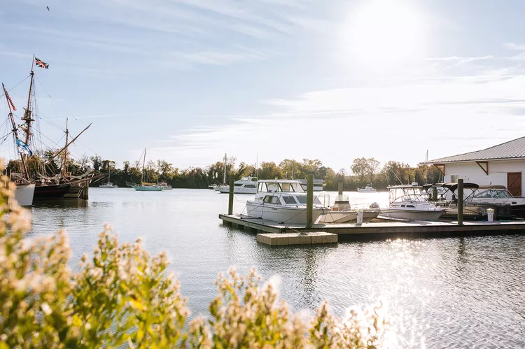 Boats tied up at a marina in Urbanna on the Rappahannock River, with a tall ship anchored in the harbor