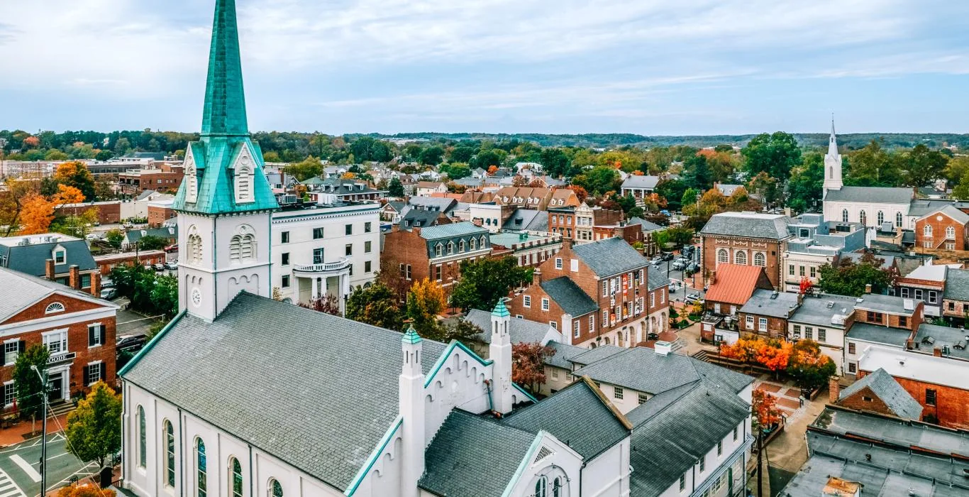 Aerial view of historic downtown Fredericksburg, Virginia in fall, with a white church and green copper steeple in front of brick storefronts and autumn trees