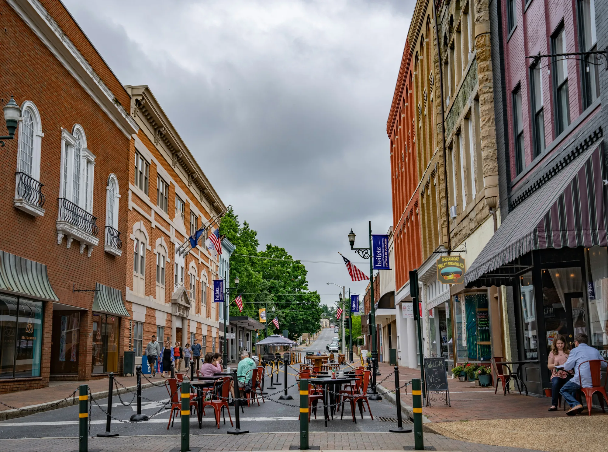 Historic brick storefronts and outdoor cafe tables along a downtown street in Staunton, Virginia, under a cloudy sky