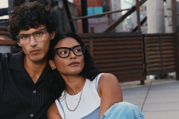 Portrait of a man in a blue shirt and a woman wearing a white tank top sitting on a city rooftop modeling McAllister glasses.