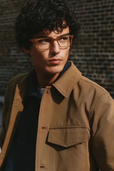 Portrait of a brown haired man wearing an orange jacket looking into the sun while wearing orange McAllister glasses.