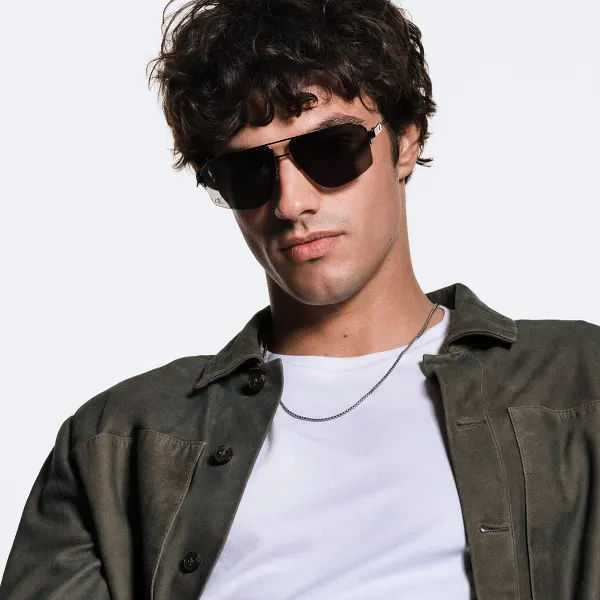 Photo of a brown haired man wearing a brown jacket over a white shirt modeling Calvin Klein sunglasses on a white background.