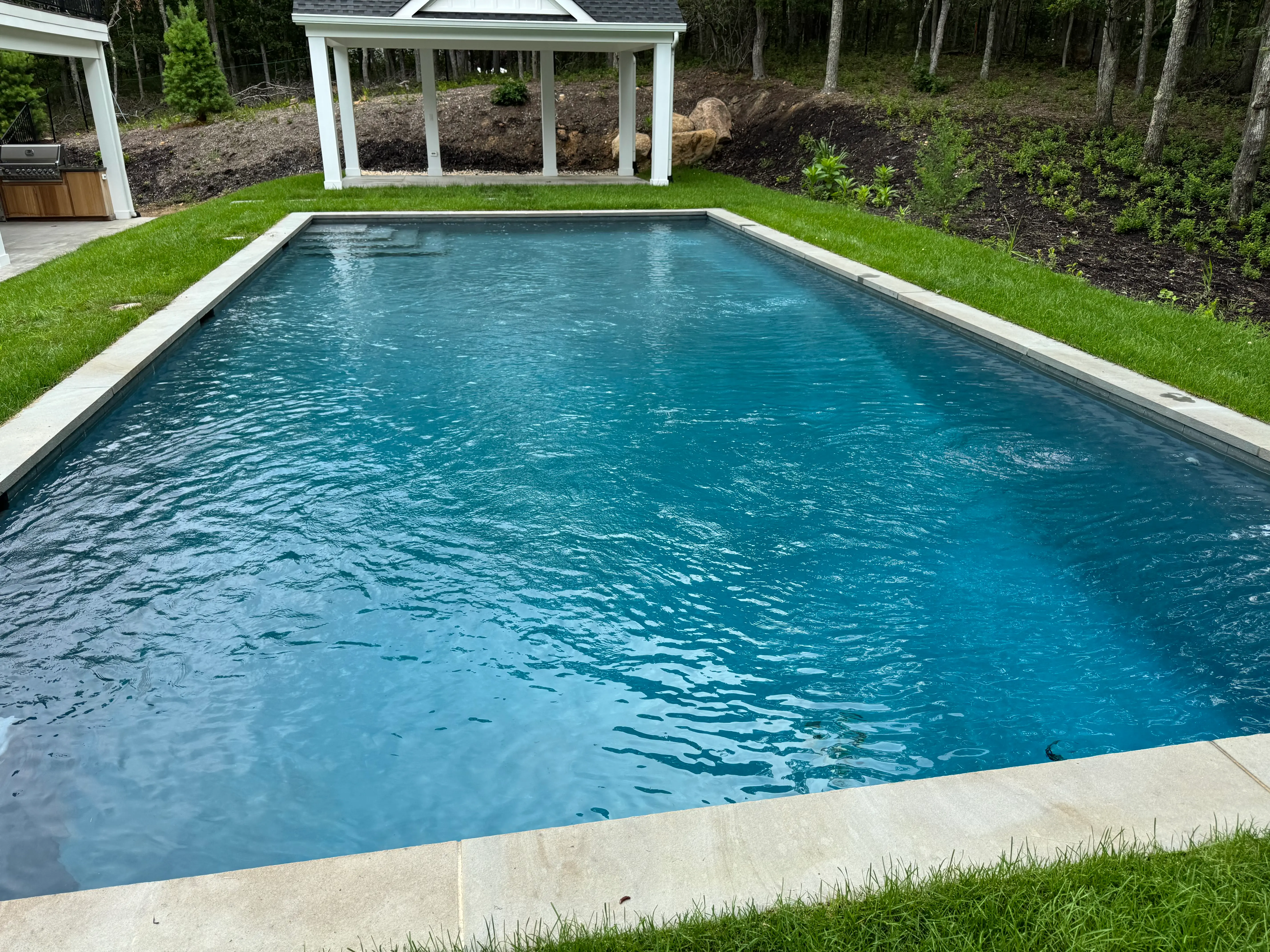 Clean in-ground pool with clear blue water, stone coping, and landscaped backyard on Long Island, NY near Hampton Bays.