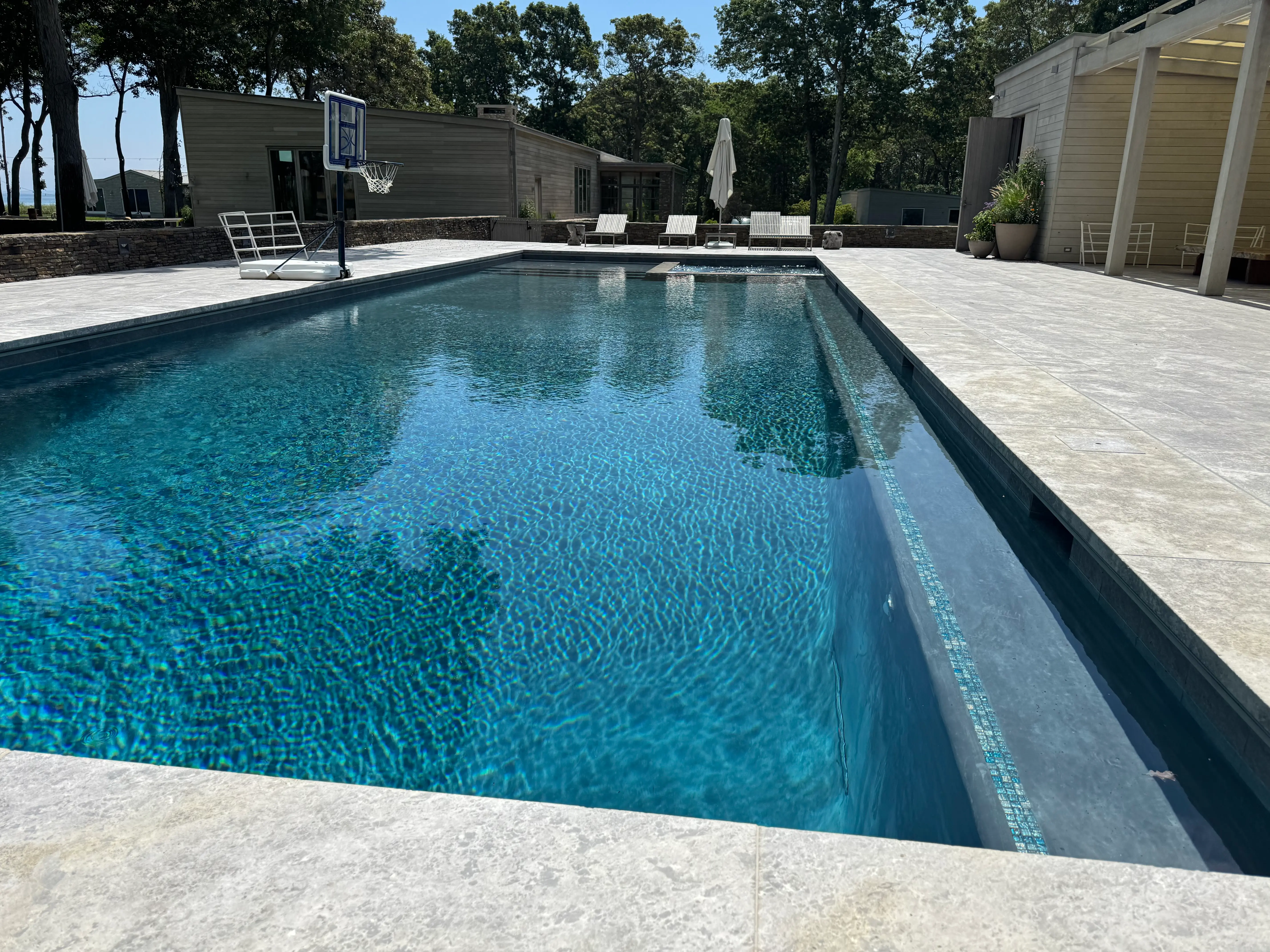Clean modern in-ground pool with clear blue water, integrated spa, and light stone patio on Long Island, NY near Remsenburg.