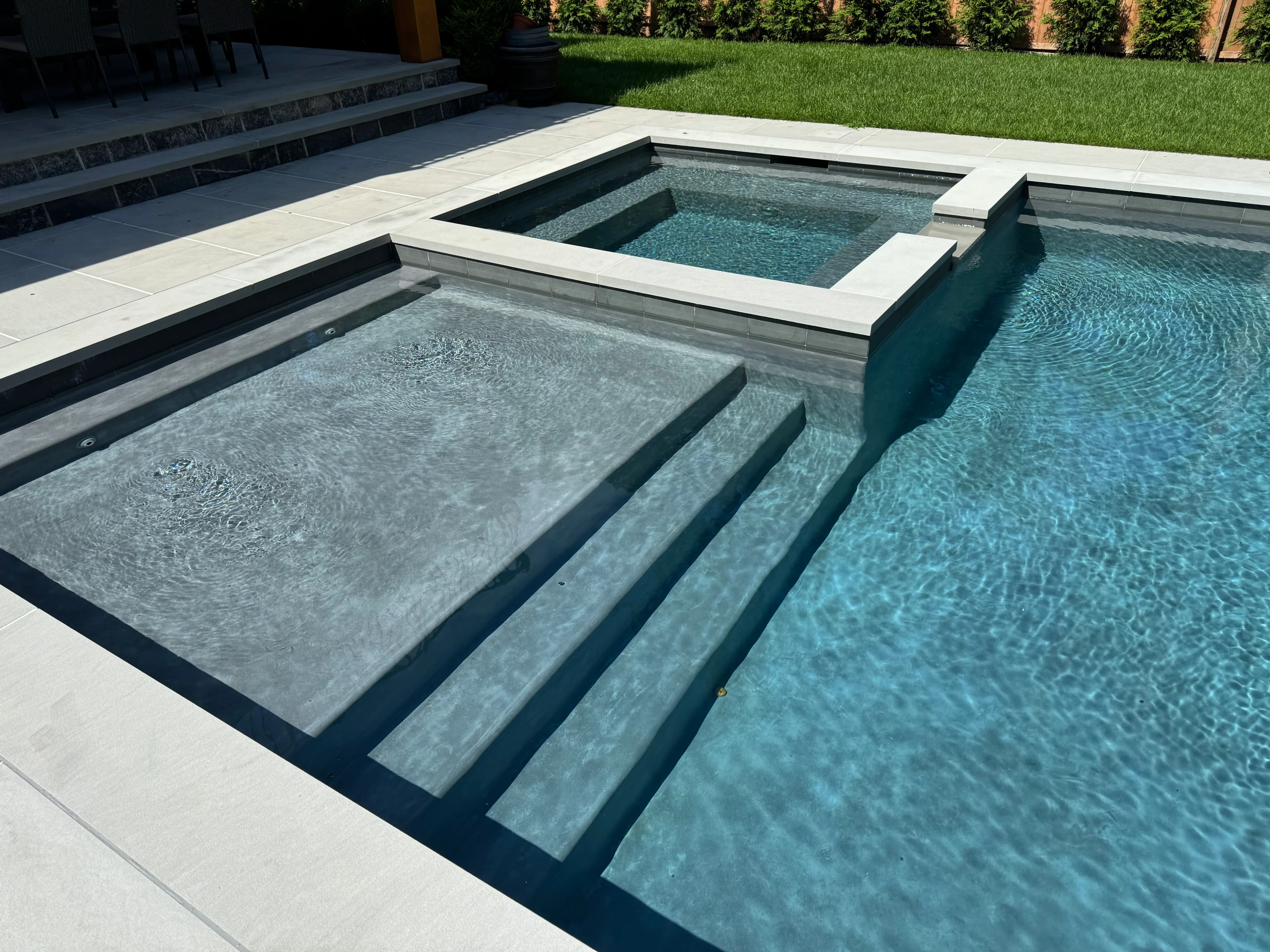 Modern in-ground pool with integrated spa, tanning ledge, built-in steps, and clear blue water on Long Island, NY near Quogue.