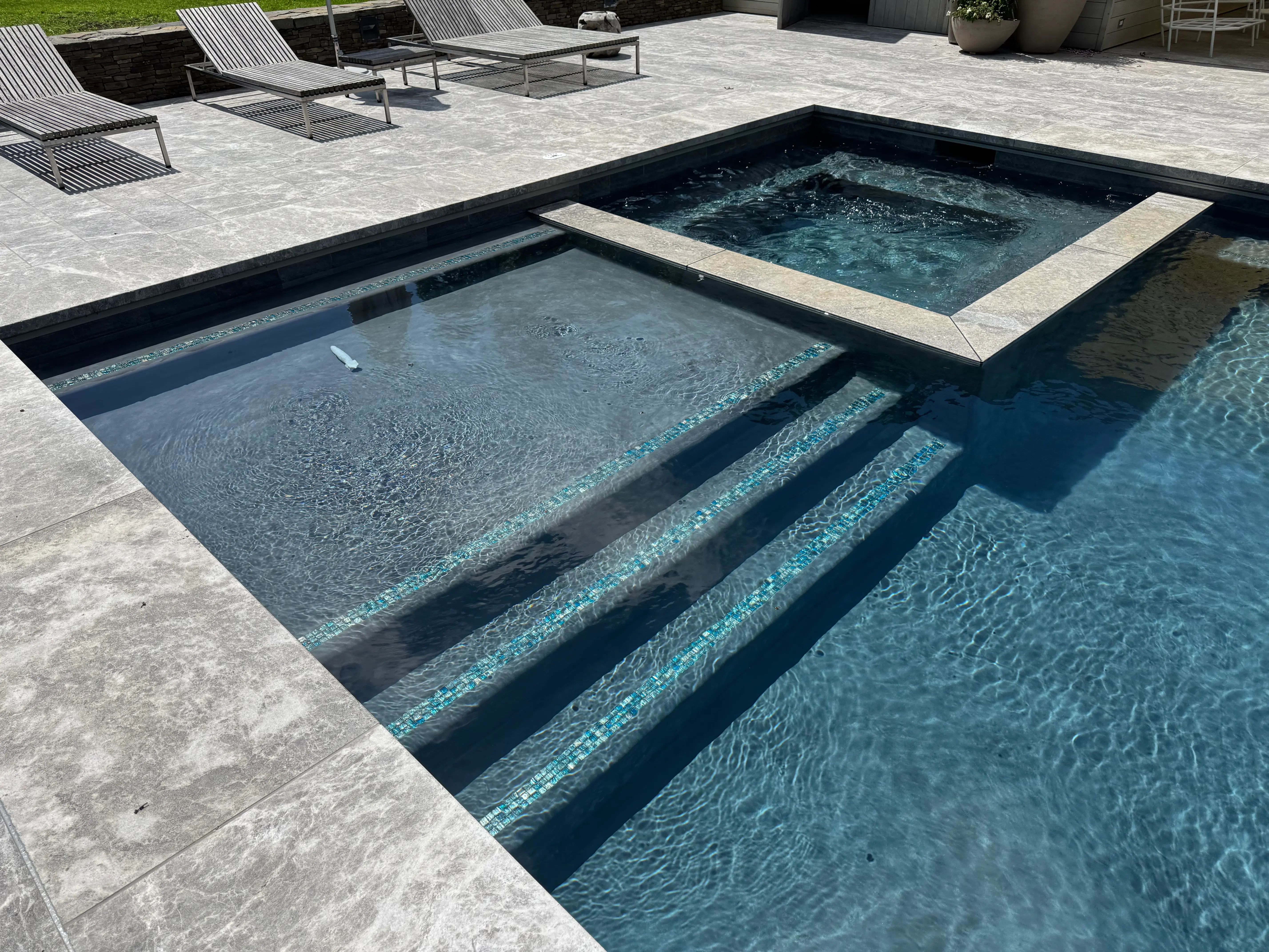 Modern in-ground pool with integrated spa, tanning ledge, built-in steps, and stone patio on Long Island, NY near Westhampton Beach.