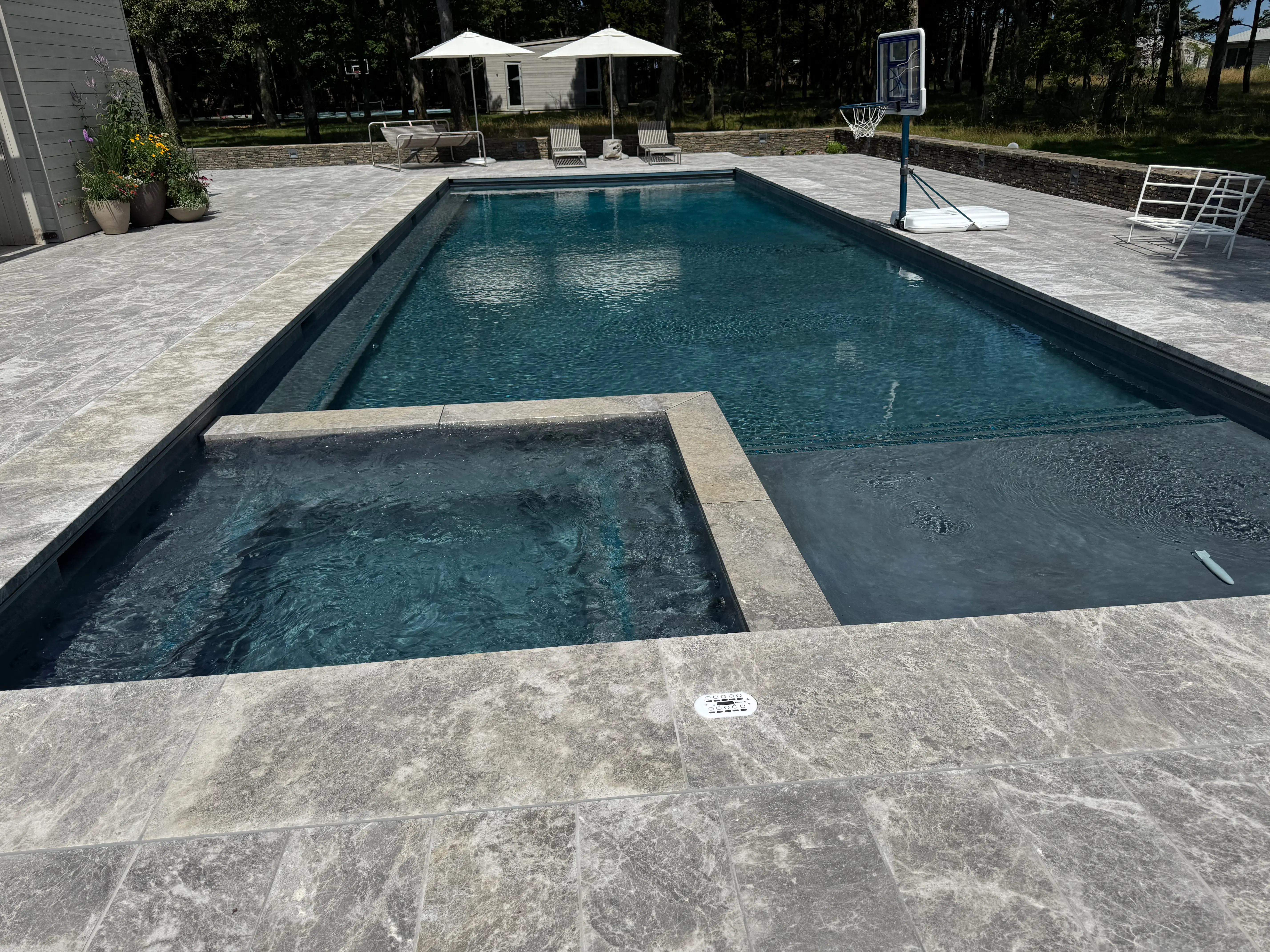 Modern in-ground pool with integrated spa, tanning ledge, clear blue water, and stone patio on Long Island, NY near Westhampton.