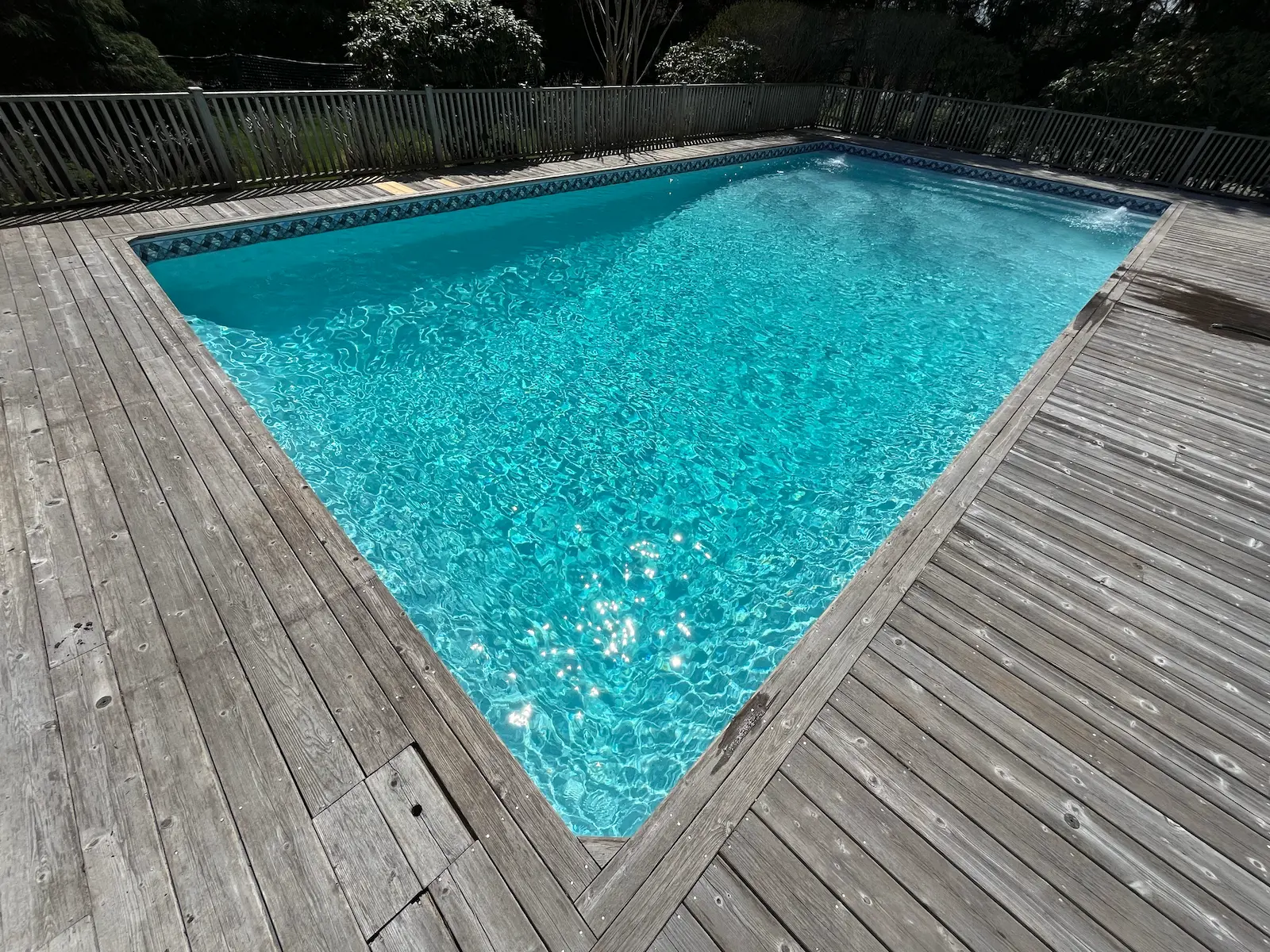 Clean in-ground pool with clear blue water and surrounding wood deck on Long Island, NY near Remsenburg.