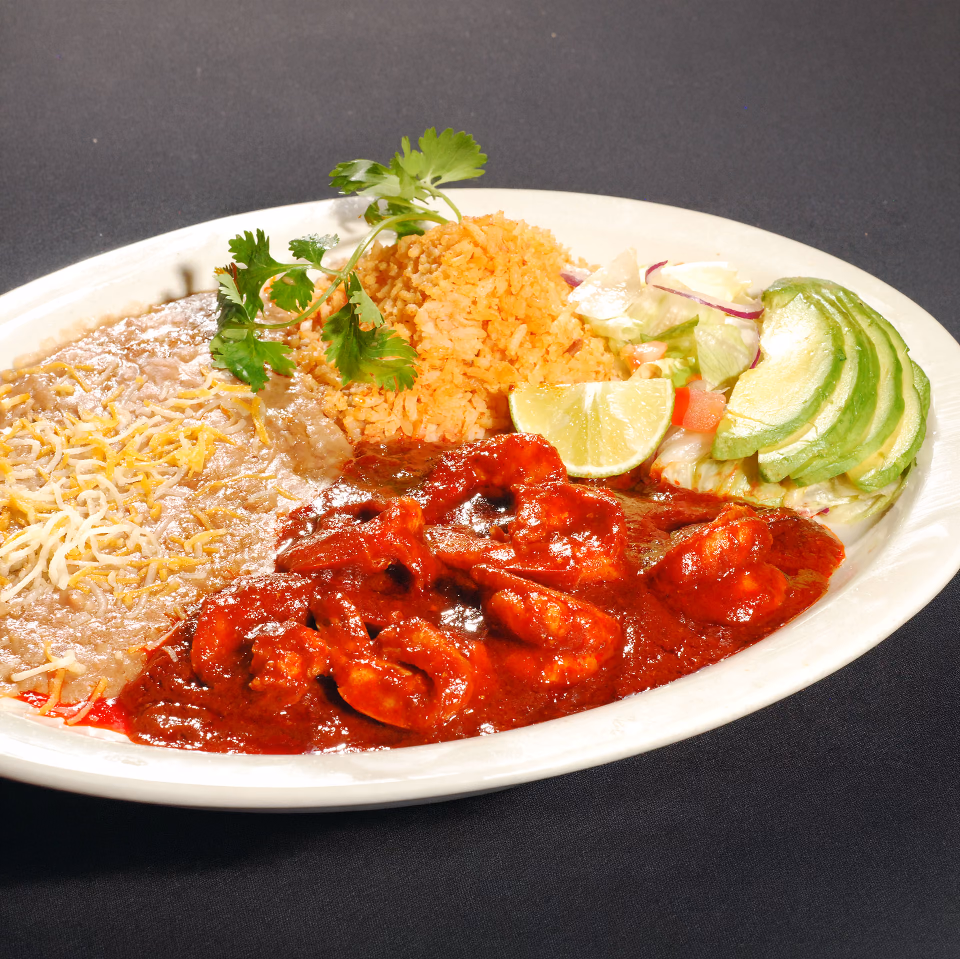 Plate of Mexican food with camarones a la diabla, refried beans, Mexican rice, avocado slices, and a salad.
