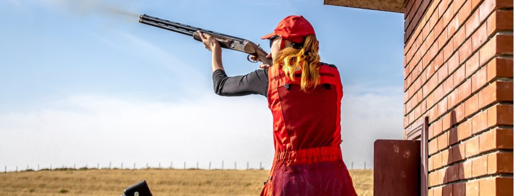 Woman in red gear aiming a shotgun during clay target shooting outdoors