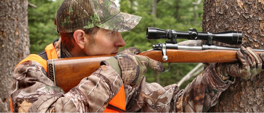 Hunter in camouflage aiming a rifle with a scope in the forest