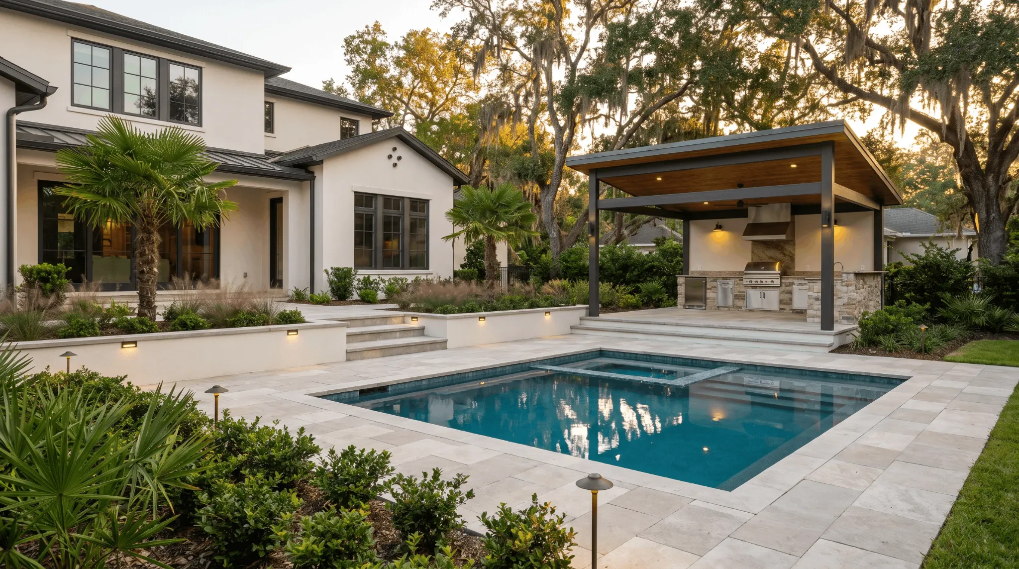 Illustrative backyard at dusk with a lit outdoor kitchen, paths and gathering areas connected to the house.