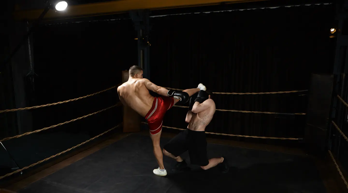 Kickboxer delivering a high kick to a sparring partner inside a training ring.