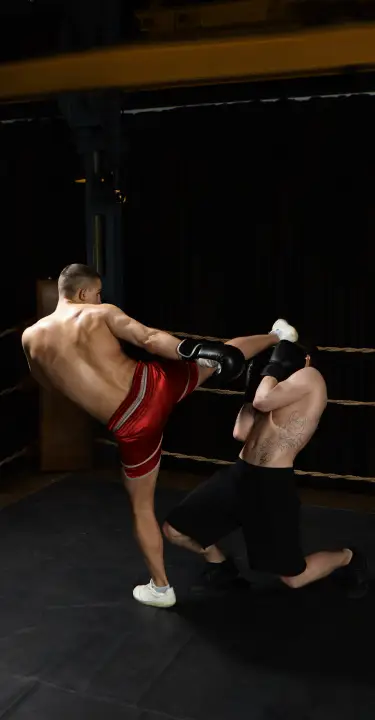 Kickboxer delivering a high kick to a sparring partner inside a training ring.