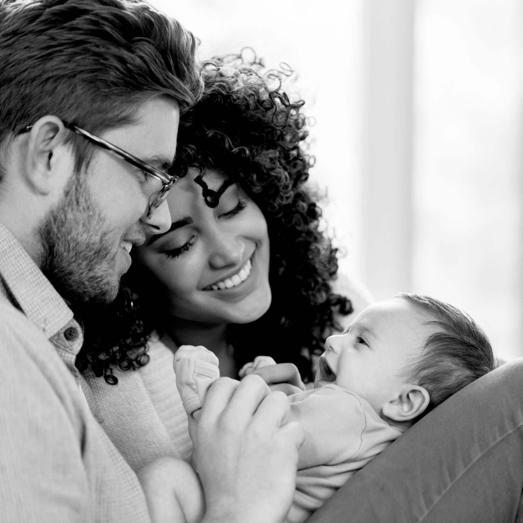Smiling parents holding and looking lovingly at their happy baby lying on a couch.