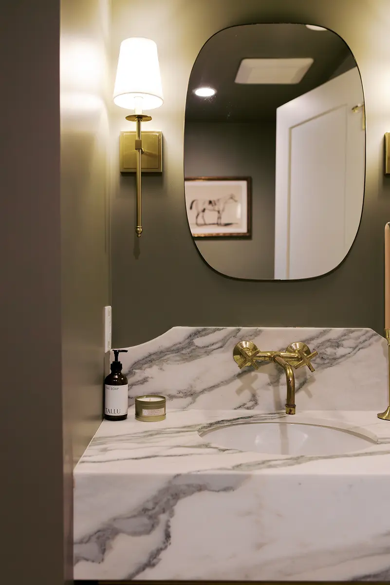 Powder room with a brass wall sconce, rounded mirror and marble sink, Pemberton Heights renovation
