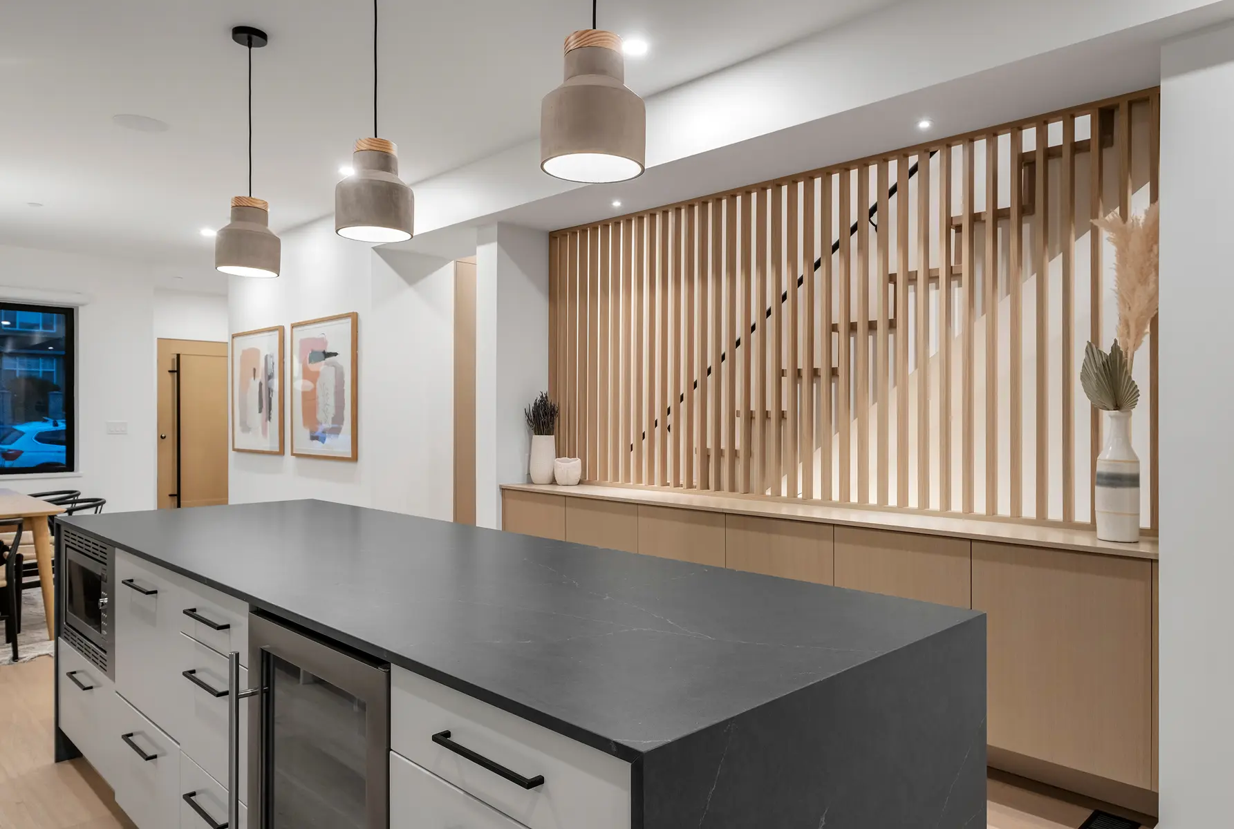 Kitchen island with dark stone counter and pendant lights beside a slatted wood stair screen, 4th Street duplex