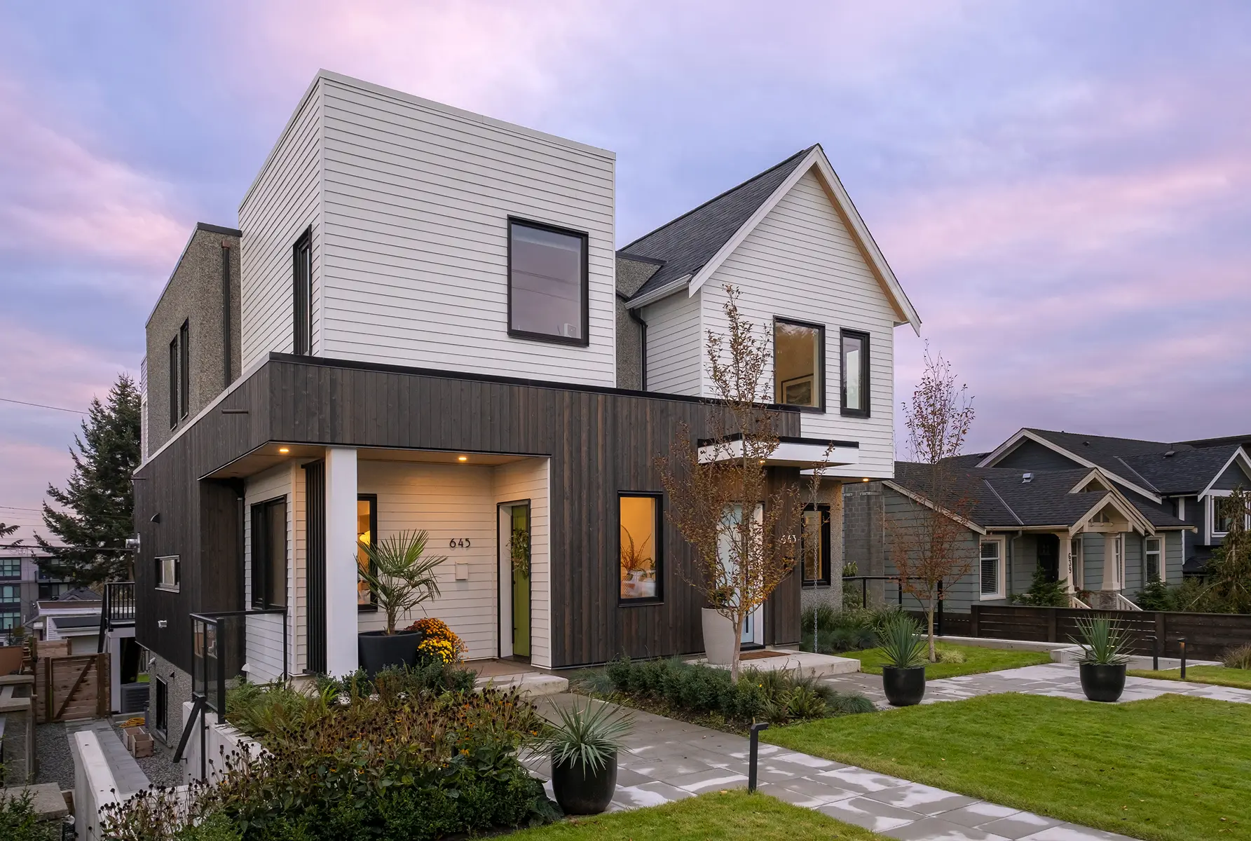 Exterior of the 4th Street duplex in North Vancouver with white siding and dark wood cladding at dusk