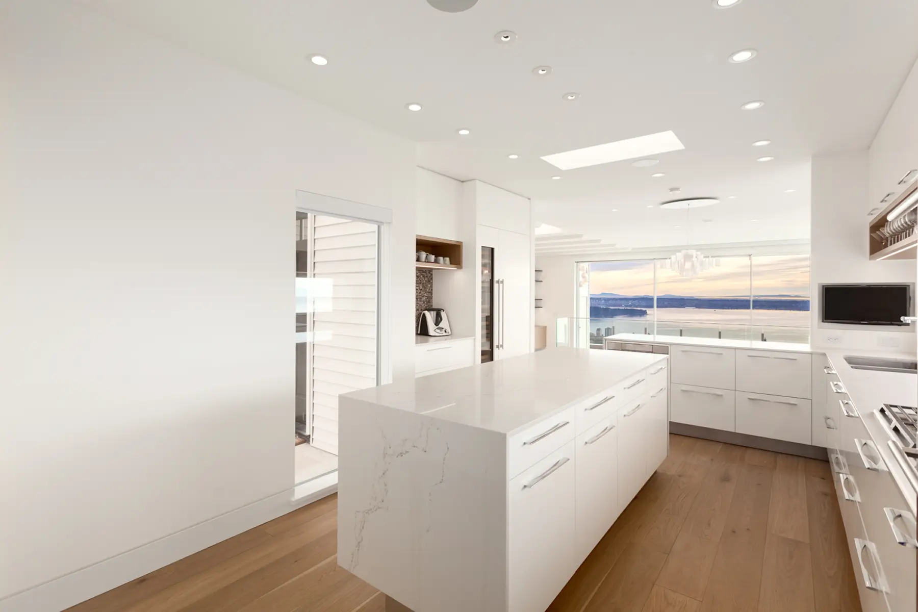 Kitchen island with a stone waterfall counter and white cabinetry, Folkstone Way rebuild in West Vancouver