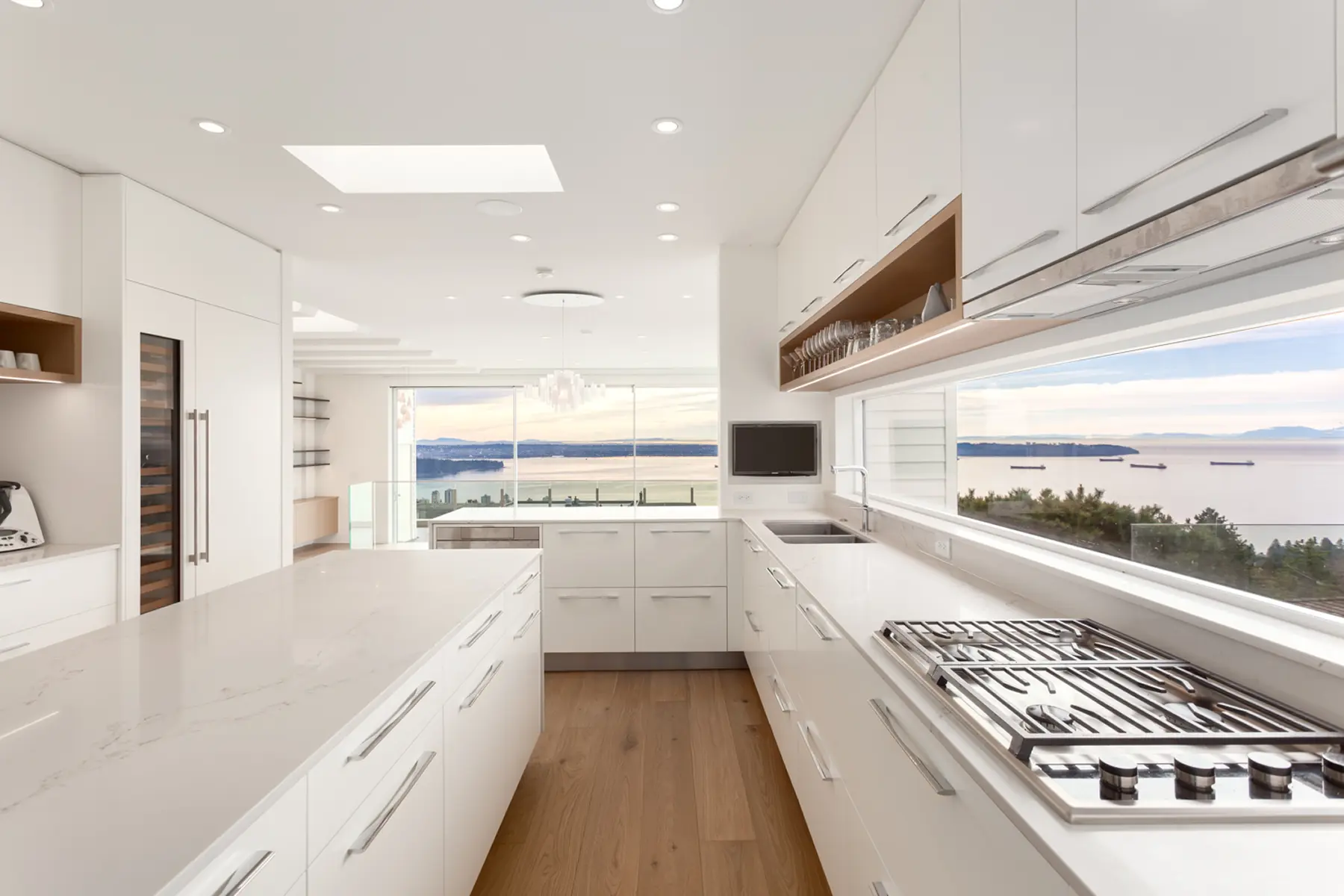 White kitchen with a long window backsplash overlooking the water, Folkstone Way rebuild in West Vancouver