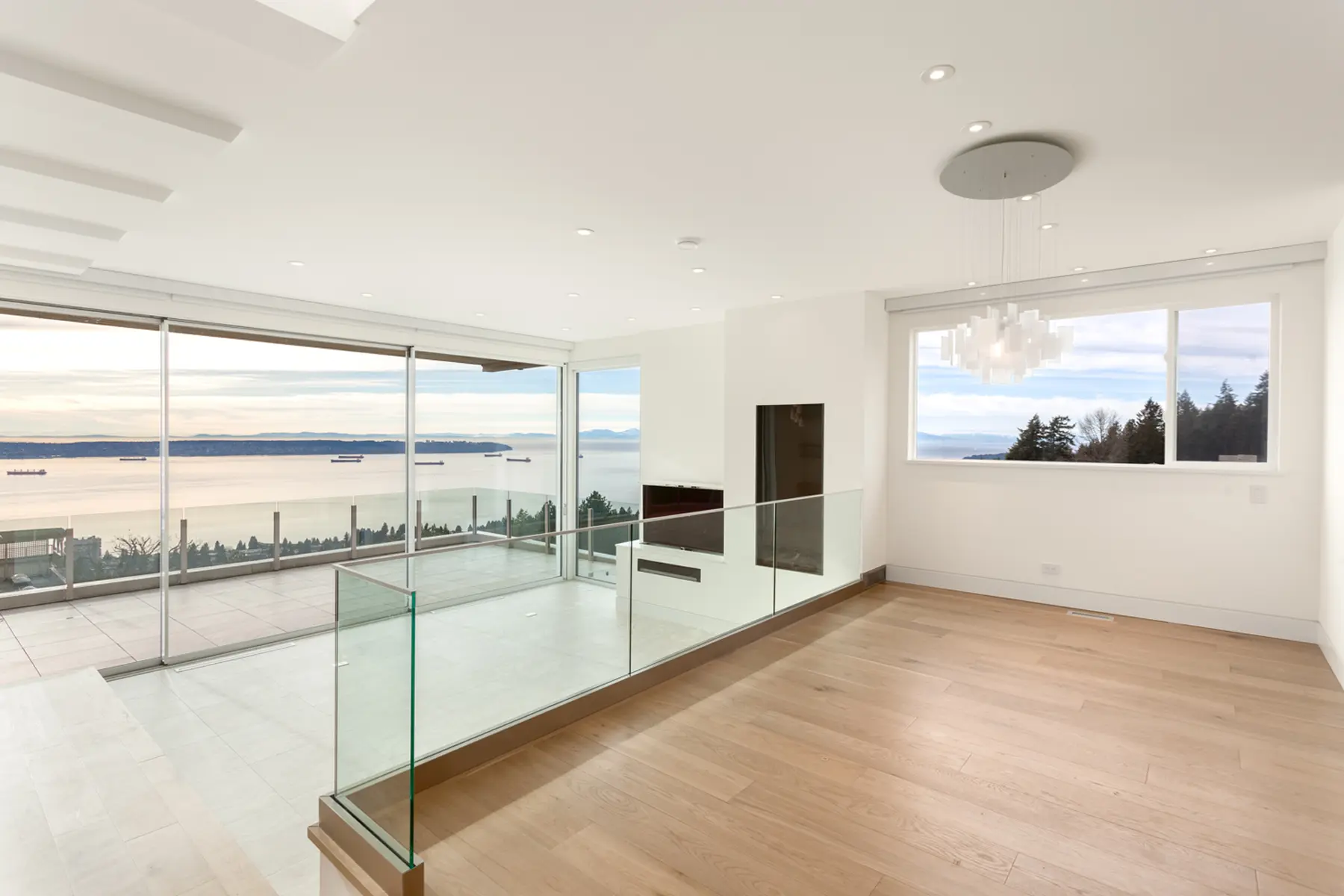 Open living room with a glass-railed balcony and sweeping water views, Folkstone Way rebuild in West Vancouver