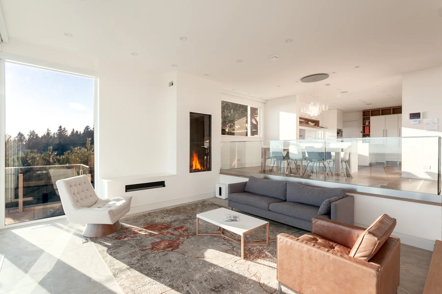 Living area with a linear fireplace, sectional seating and a large window onto tall evergreens, Folkstone Way rebuild in West Vancouver