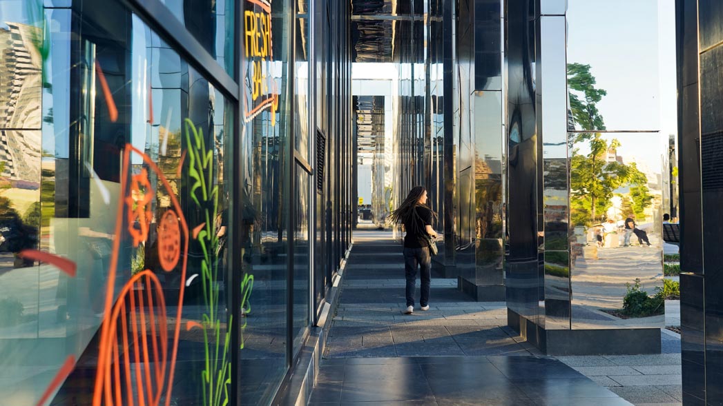 Woman walking past a mirrored office building on a city street