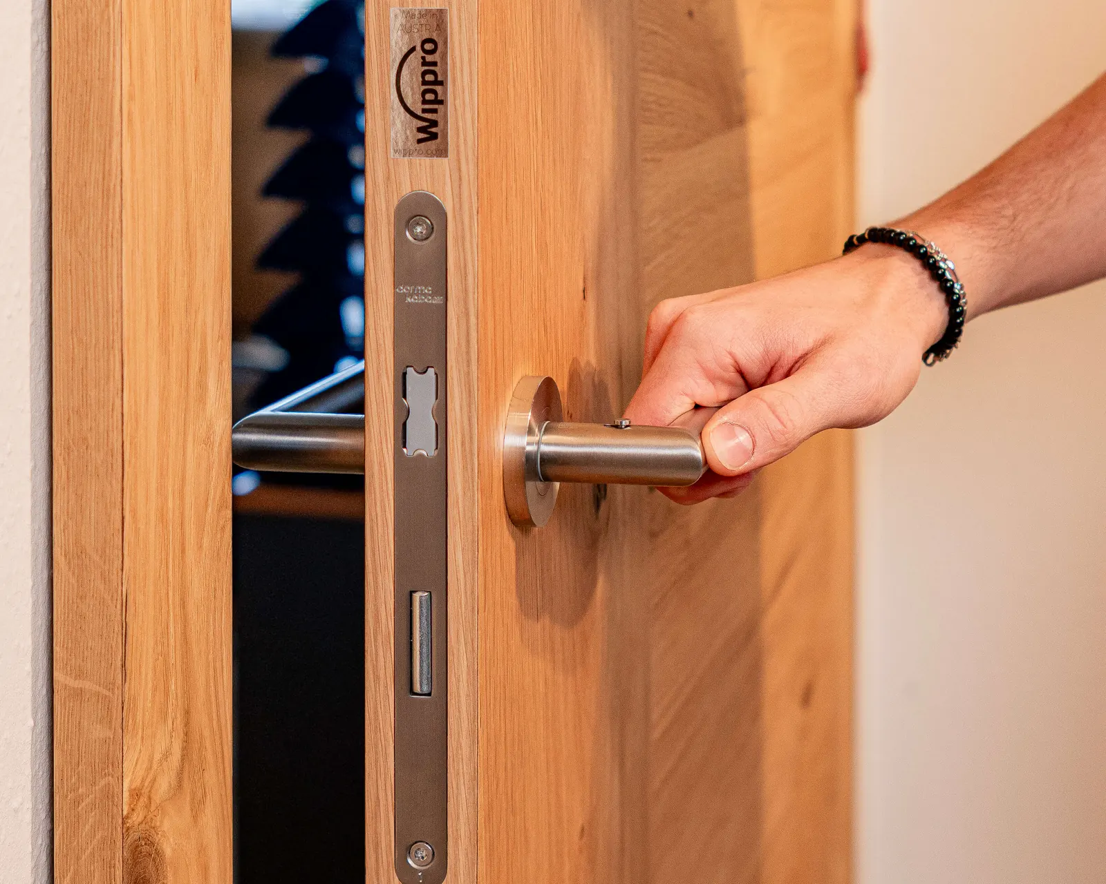 Hand öffnet eine Massivholz-Innentür von Wippro mit Edelstahlgriff