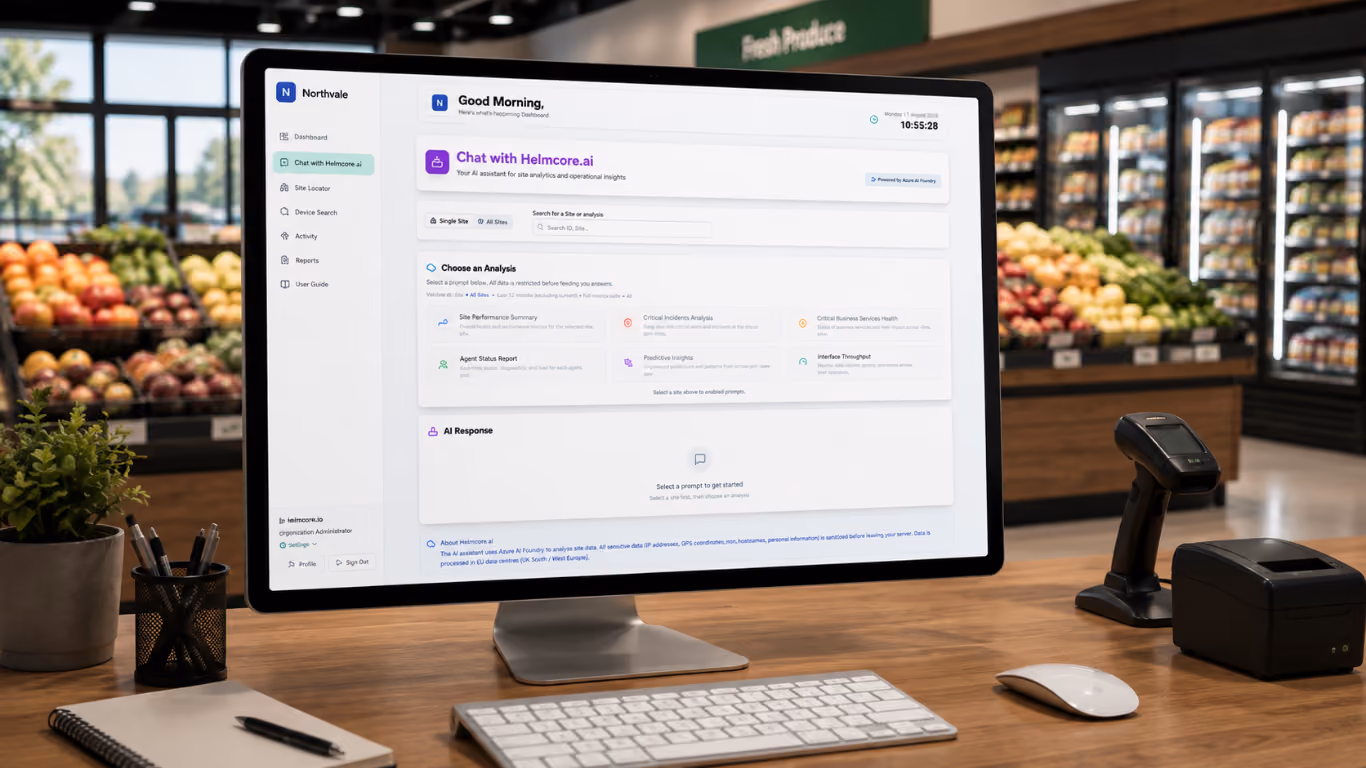 Desktop computer on a wooden desk displaying a dashboard of Helmcore.ai, an AI assistant for site analytics and operational insights, with options for different analyses. The desk also has a keyboard, mouse, barcode scanner, receipt printer, pen holder, and a notebook with a pen. The background shows a grocery store produce section with fruits and vegetables.