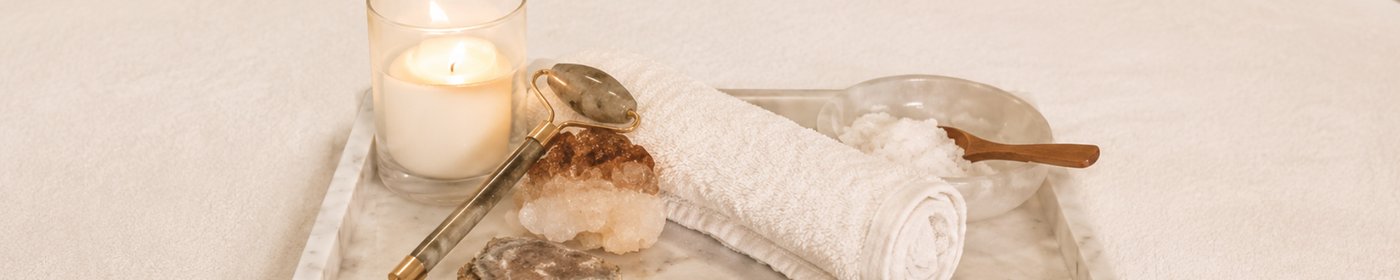 A spa ritual tray with candle, jade roller, rolled towel, and salt scrub