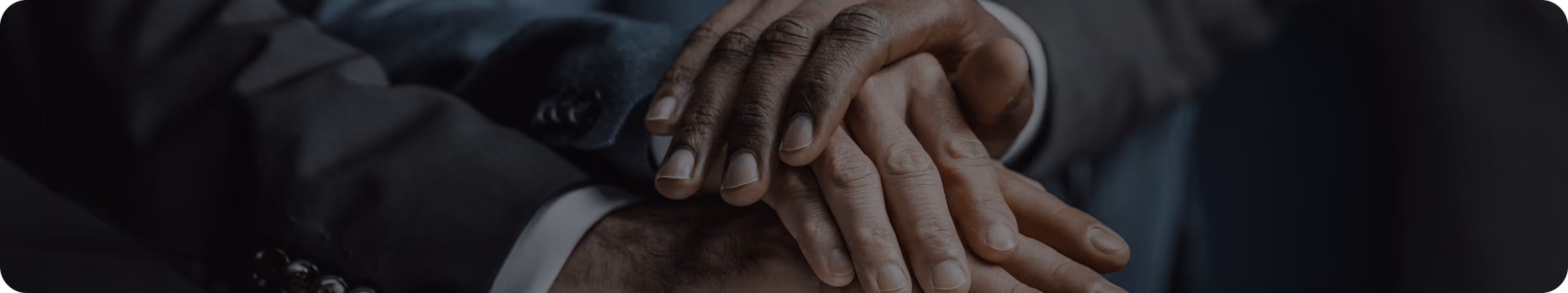 Close-up of two people holding hands in a gesture of support or solidarity, one hand darker-skinned and the other lighter-skinned, both wearing formal clothing.