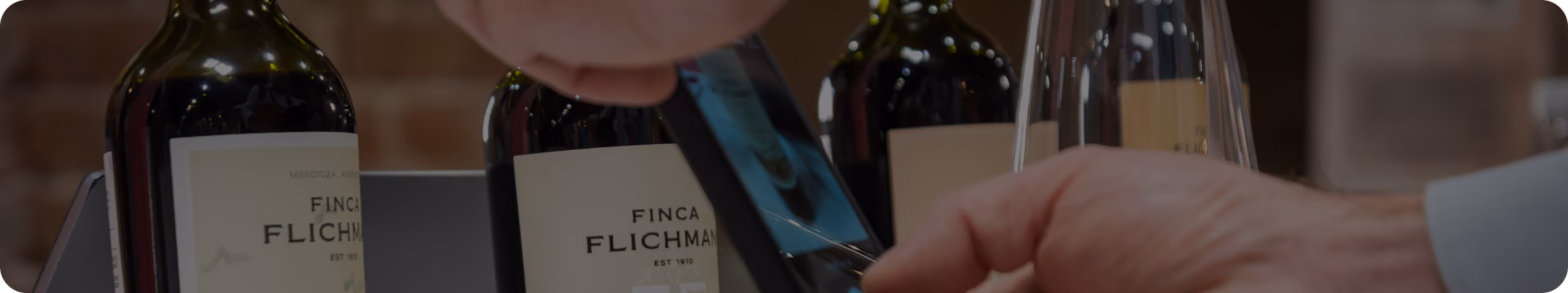 Close-up of hands opening a bottle of red wine labeled Finca Flichman with other wine bottles and glasses blurred in the background.