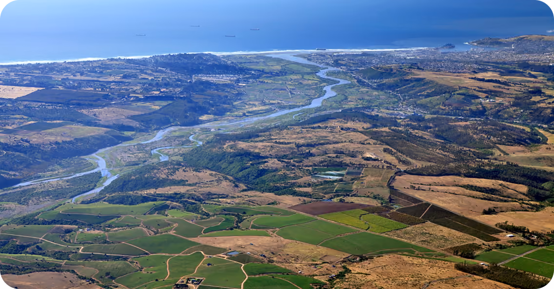 Aerial view of a coastal landscape featuring winding rivers flowing through green and brown agricultural fields towards the ocean under a clear blue sky.