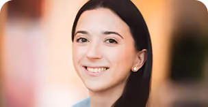 Portrait of a young woman with long dark hair, smiling and looking at the camera, wearing pearl earrings.