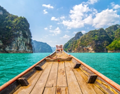 Boat bow facing turquoise water with green limestone cliffs under a blue sky with clouds.
