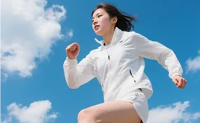 Woman in a white jacket and shorts running outdoors against a bright blue sky with scattered clouds.