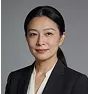 Professional portrait of an Asian woman with dark hair tied back, wearing a black blazer and white top, smiling gently against a plain white background.