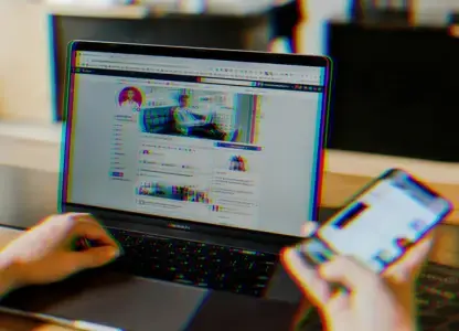 Person scrolling social media on a phone in front of a laptop