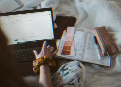Person typing on a laptop beside a notebook and colour swatches