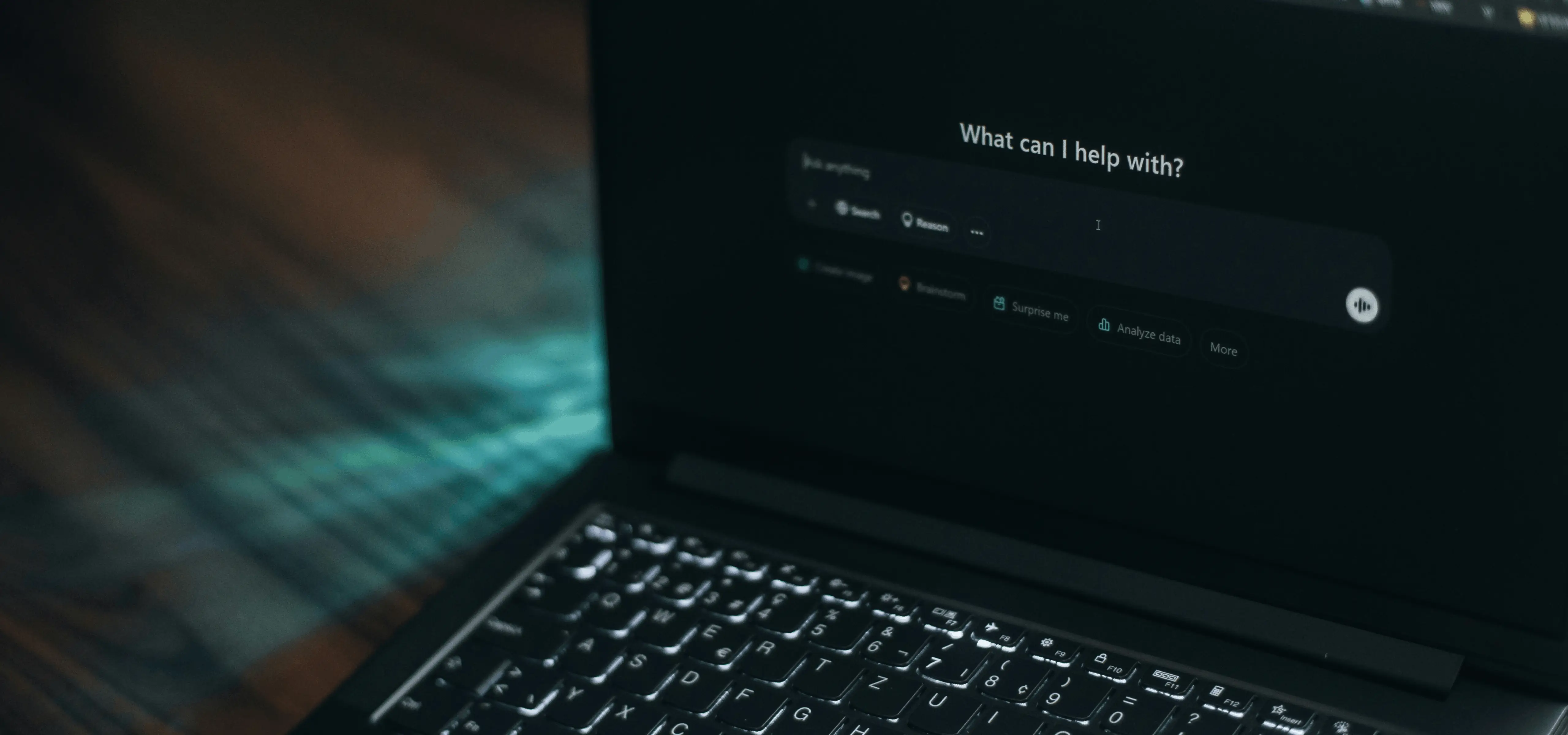 Laptop in a dark room showing an AI chat screen that asks What can I help with?
