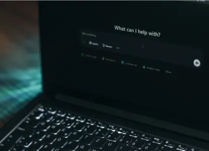 Laptop in a dark room showing an AI chat screen that asks What can I help with?