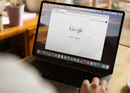 Person using a laptop showing the Google homepage, with a cup of coffee on the table
